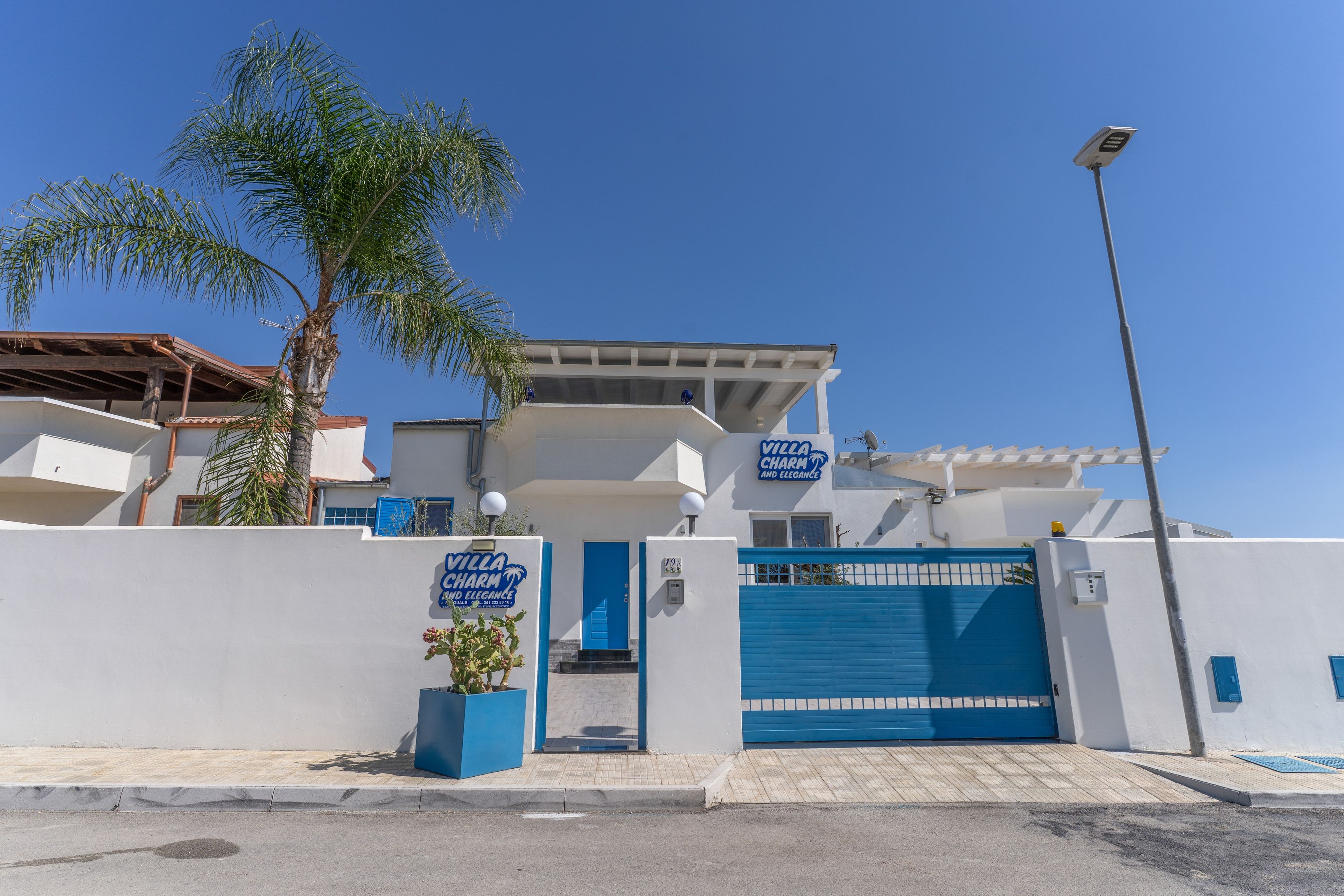 A villa with a blue gate, palm trees, and a clear sky.