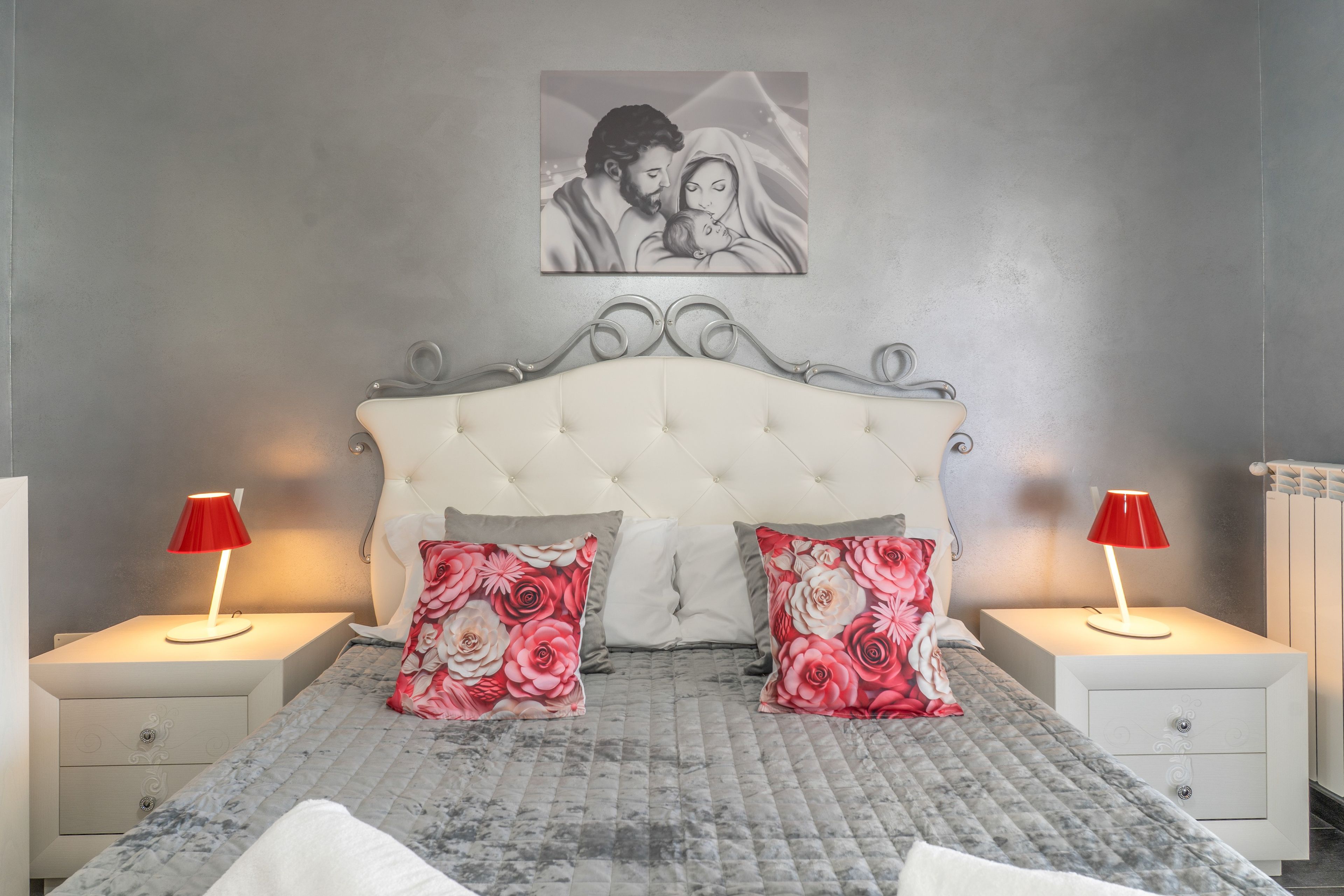 Une chambre à coucher avec une tête de lit capitonnée, deux lampes de chevet et des coussins à motifs floraux.
