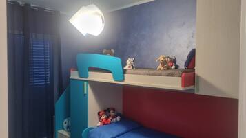 En køjeseng med skrivebord og hylder, en hængende lampe og et vindue med skodder.