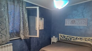 Une chambre à coucher comprenant un lit, une table de chevet, une fenêtre avec des rideaux, un radiateur et un panneau décoratif mural.