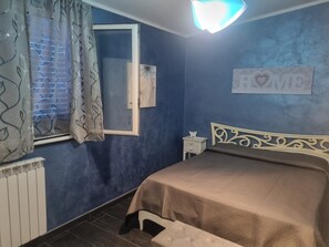 Een slaapkamer met een bed, een nachtkastje, een raam met gordijnen, een radiator en een bord aan de muur.