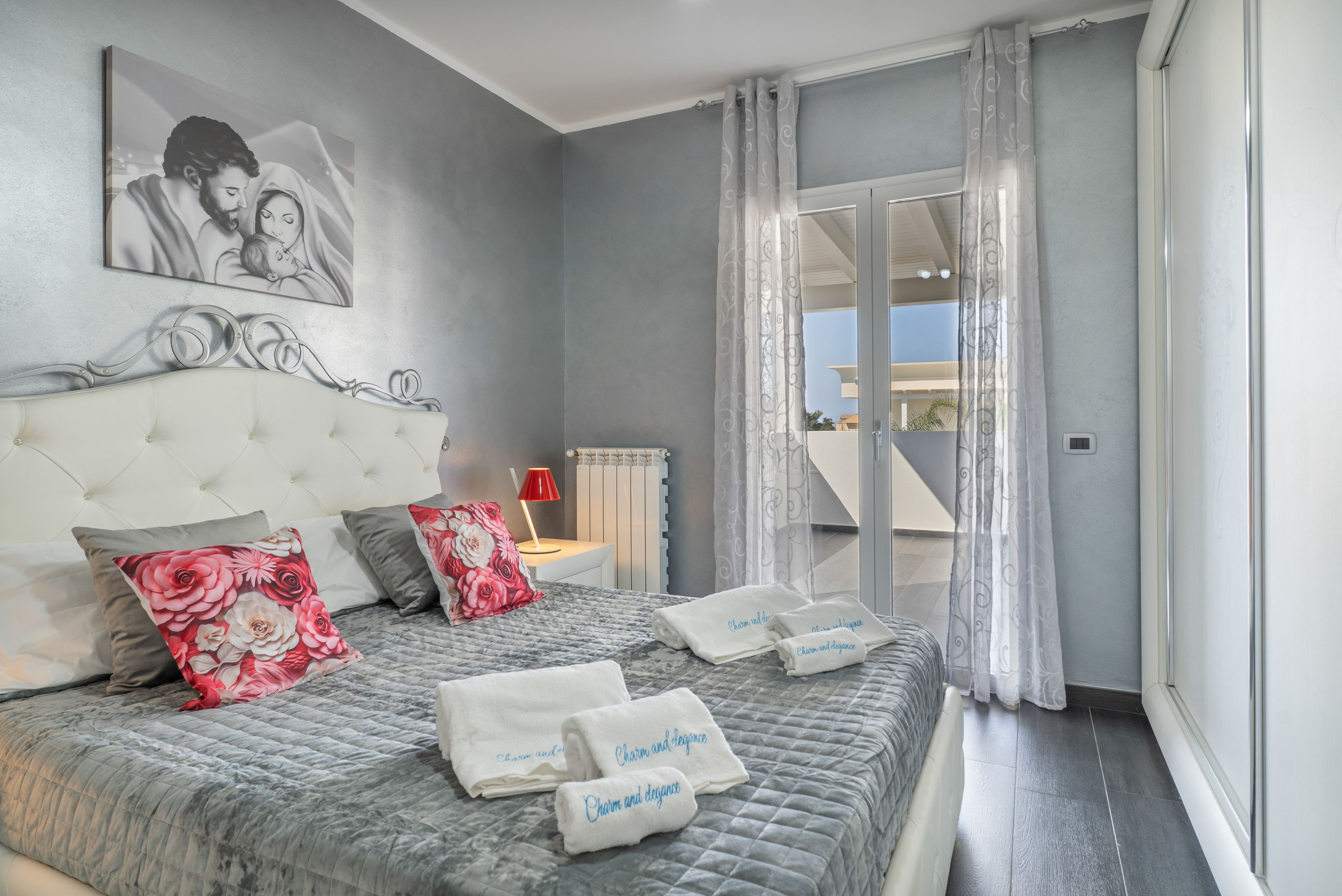 A bedroom with a large bed, a headboard, a nightstand, a lamp, and a view of the outside.