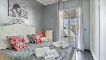 A bedroom with a large bed, a headboard, a nightstand, a lamp, and a view of the outside.