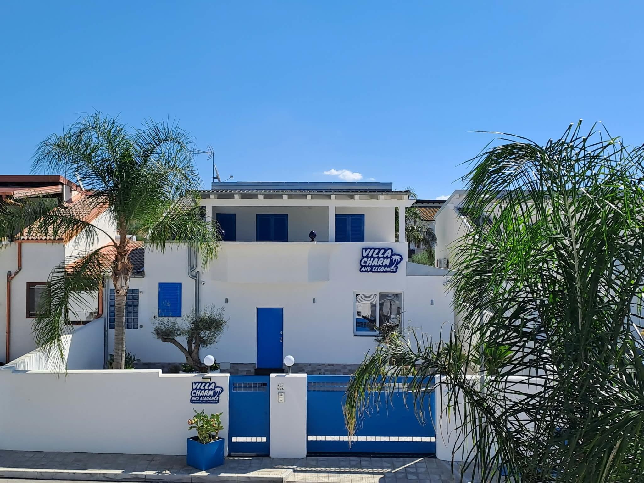 A two-story building with a blue door and windows, surrounded by palm trees and a clear sky.