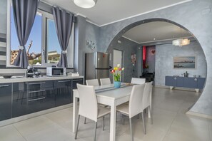A modern kitchen with a dining area, featuring a large window, grey walls, and a view of the outdoors.