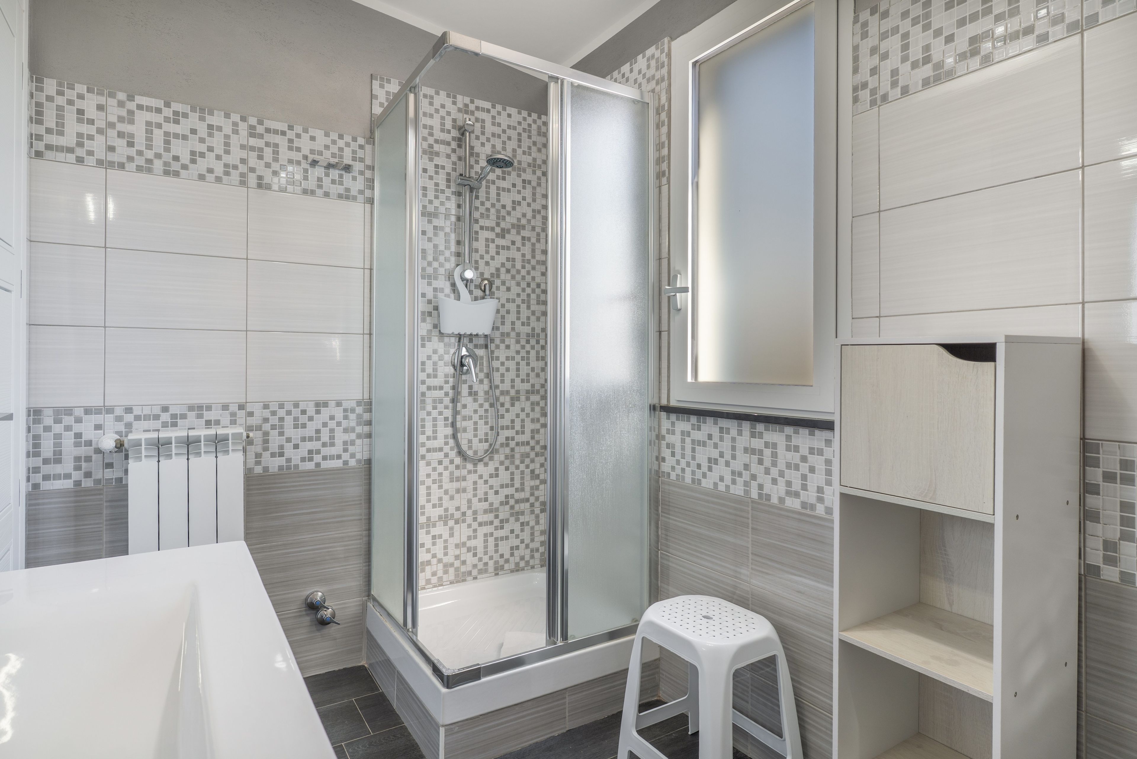 A modern bathroom with a glass-enclosed shower, a white sink, and tiled walls.
