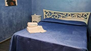 Ein Schlafzimmer mit blauer Wand, einem Bett mit dekorativer Kopfteil, einem Nachttisch mit Lampe und einem Gemälde.