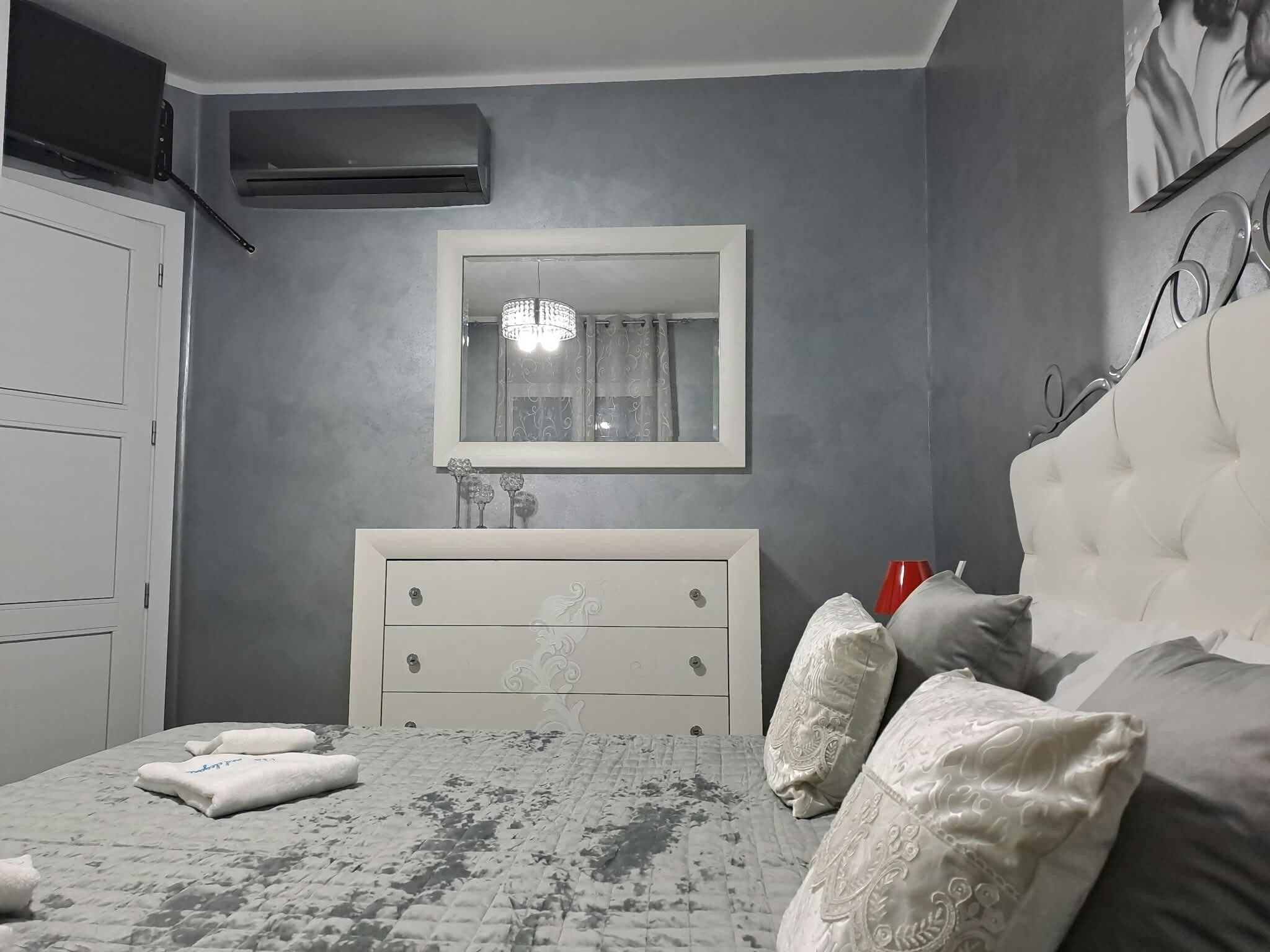 Una camera da letto con un letto, una cassettiera, uno specchio e una tazza rossa sul comodino.