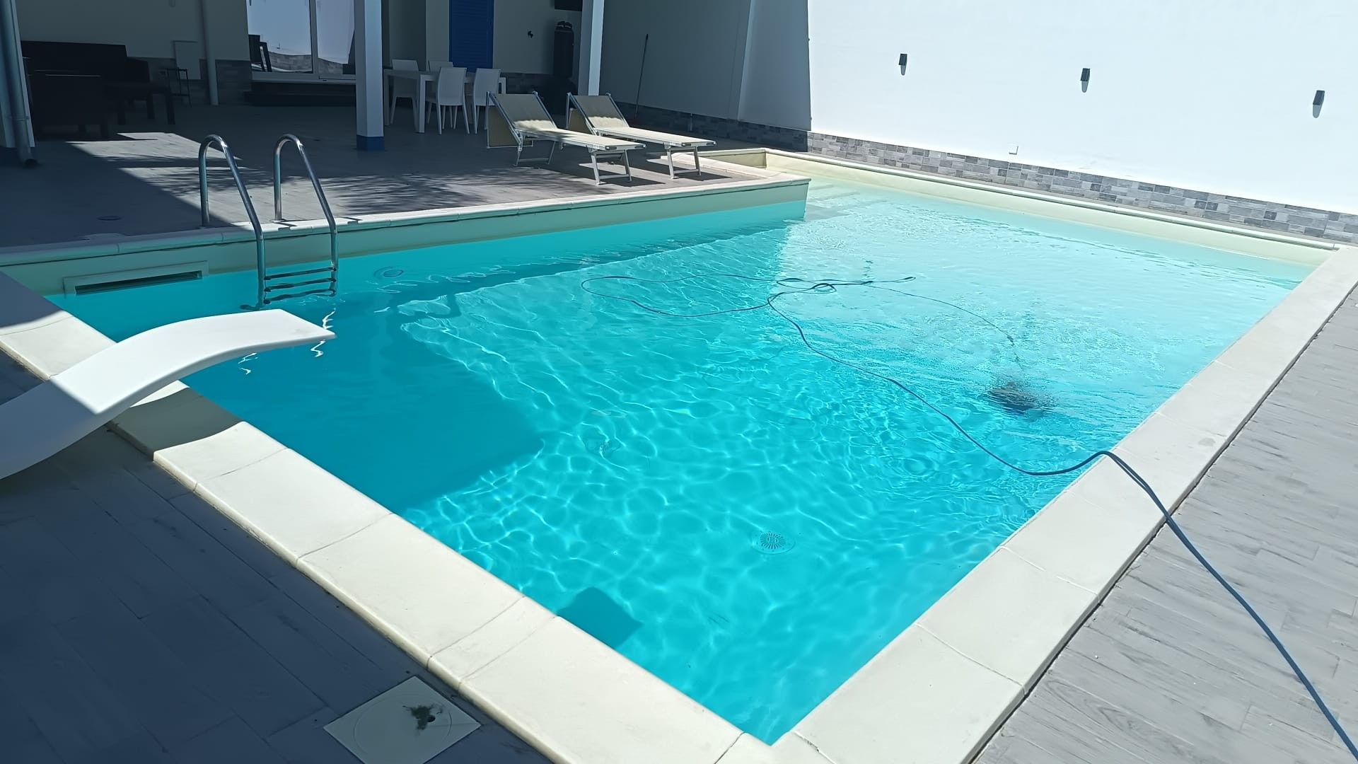 Ein Swimmingpool mit glatter, blauer Wasseroberfläche, umgeben von einer gefliesten Liegefläche und Liegestühlen.