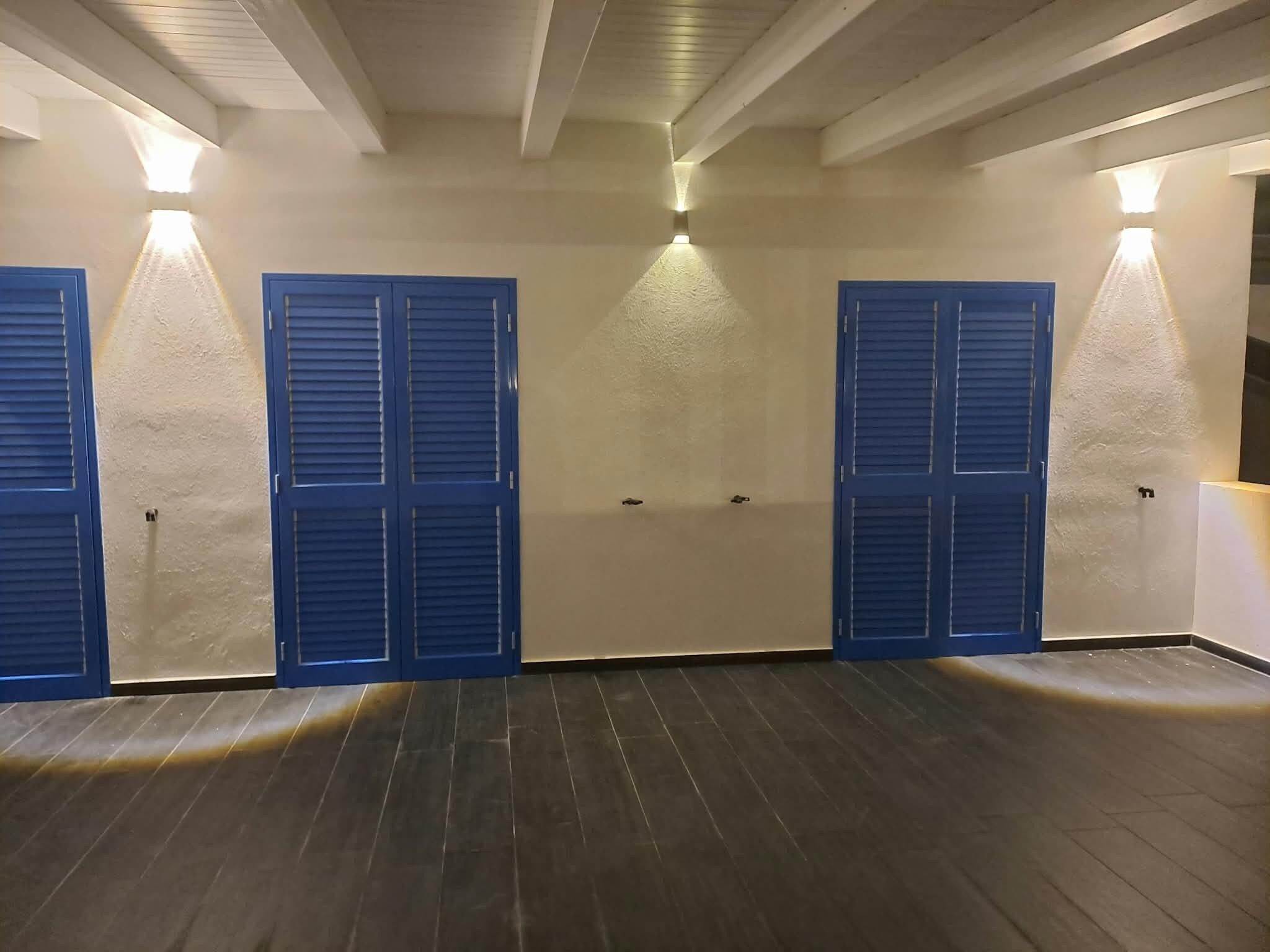 A room with a wooden floor, three blue doors, and wall-mounted lights.