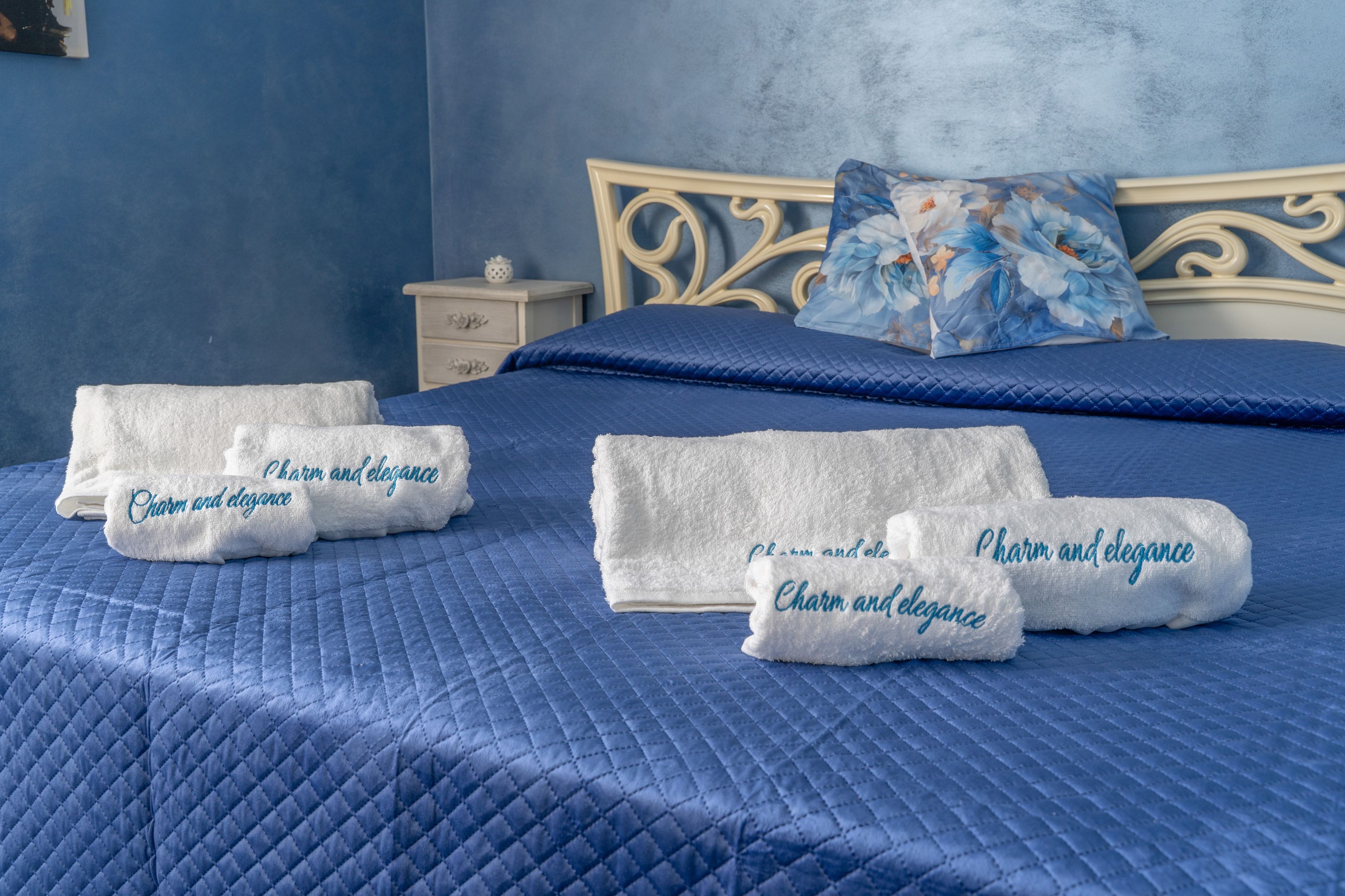 A neatly made bed with blue bedding and white towels with embroidered text.