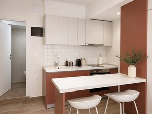 Cozinha moderna com armários brancos, bancada clara e dois bancos altos brancos.