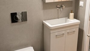 Ein modernes Badezimmer mit Toilette, Waschbecken, Spiegel und Mülleimer.