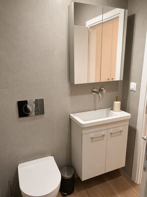 Uma casa de banho moderna com sanita, lavatório, espelho e um cesto de lixo.