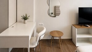 Ein modernes Wohnzimmer mit einem weißen Sofa, einem runden Holztisch, einem Fernseher auf einem Holzgestell und einem an der Wand befestigten Spiegel.