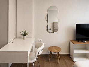 Uma sala de estar moderna com um sofá branco, uma mesa redonda de madeira, uma televisão em um móvel de madeira e um espelho fixado na parede.