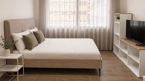 Ein modernes Schlafzimmer mit einem Bett, einem Fernseher auf einem Schrank und einem Fenster mit Vorhängen.