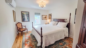 A bedroom with a four-poster bed, a chair, a rug, and framed artwork on the walls.