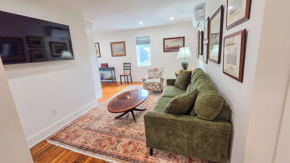 A living room with a green sofa, a wooden coffee table, a patterned rug, and a flat-screen TV mounted on the wall.