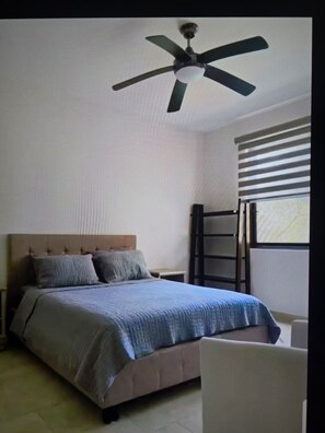 Ein Schlafzimmer mit Bett, Deckenventilator, Fenster mit Jalousien und Nachttisch.