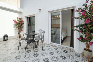 Eine Terrasse mit Tisch und Stühlen, einem Blumentopf und einer Glastür, die zu einem Schlafzimmer führt.