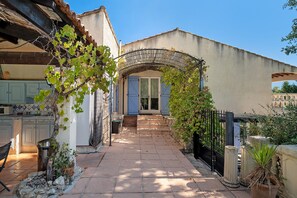 A paved pathway leading to a house with a covered entrance, a visible kitchen area, and a stone wall. - Villa 'L'escale Au Soleil' with Private Pool, Wi-Fi and Air Conditioning (Montauroux)