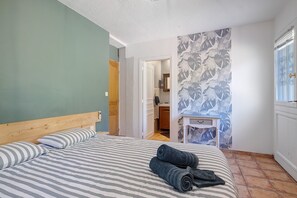 A bedroom with a bed, a wooden headboard, a bathroom with a shower, and a wall with a leaf pattern. - Villa 'L'escale Au Soleil' with Private Pool, Wi-Fi and Air Conditioning (Montauroux)