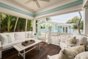 Eine überdachte Veranda mit einem weißen Sofa, einem kleinen Tisch und einem Sessel.