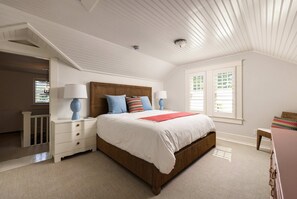 Ein Schlafzimmer mit einem großen Bett, weißen Wänden, einem hölzernen Kopfteil und einem Fenster mit Jalousien.