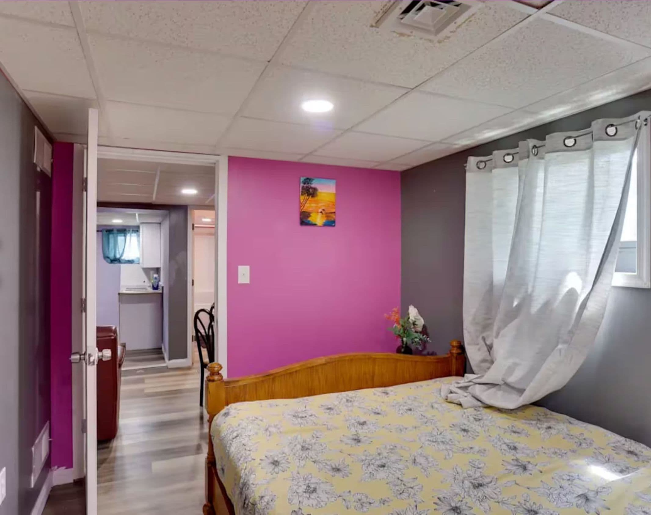 Bedroom with a wooden bed, bright pink accent wall, and a view into the adjoining room.