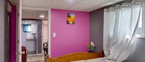 Bedroom with a wooden bed, bright pink accent wall, and a view into the adjoining room.