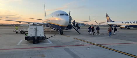 An airport tarmac with a parked airplane, ground service vehicles, and passengers boarding.