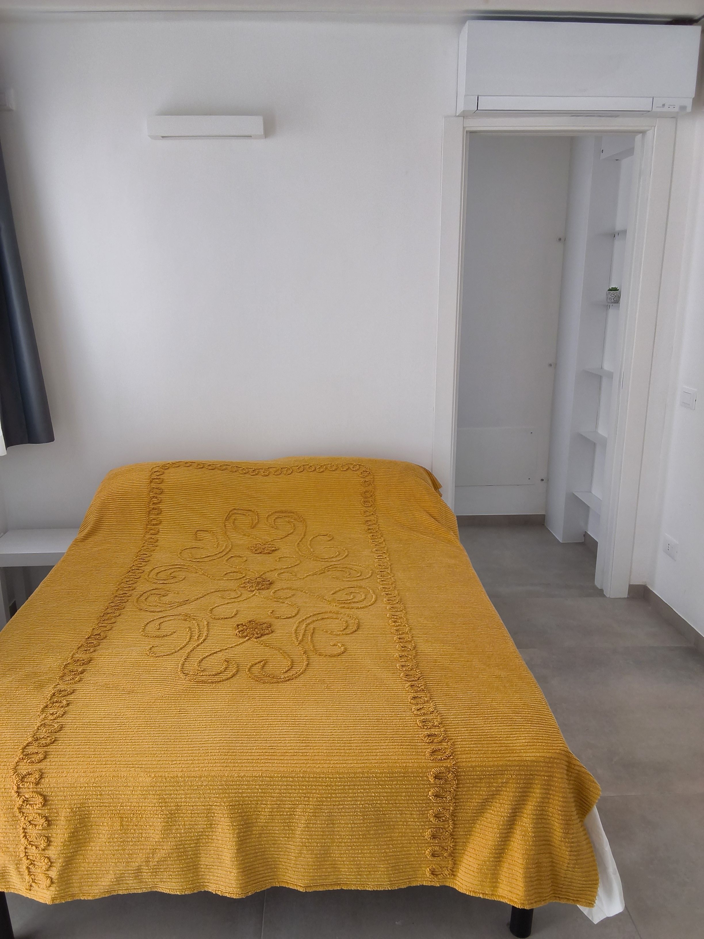 Une pièce avec un lit recouvert d’une couvre-lit jaune, une armoire blanche et une porte blanche donnant sur une autre pièce.