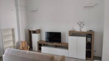A modern living room with a flat-screen TV, wooden entertainment unit, and a sofa.