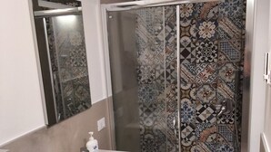 Ein Badezimmer mit weißem Waschbecken, einer Duschkabine aus Glas und einer Fliesenwand.