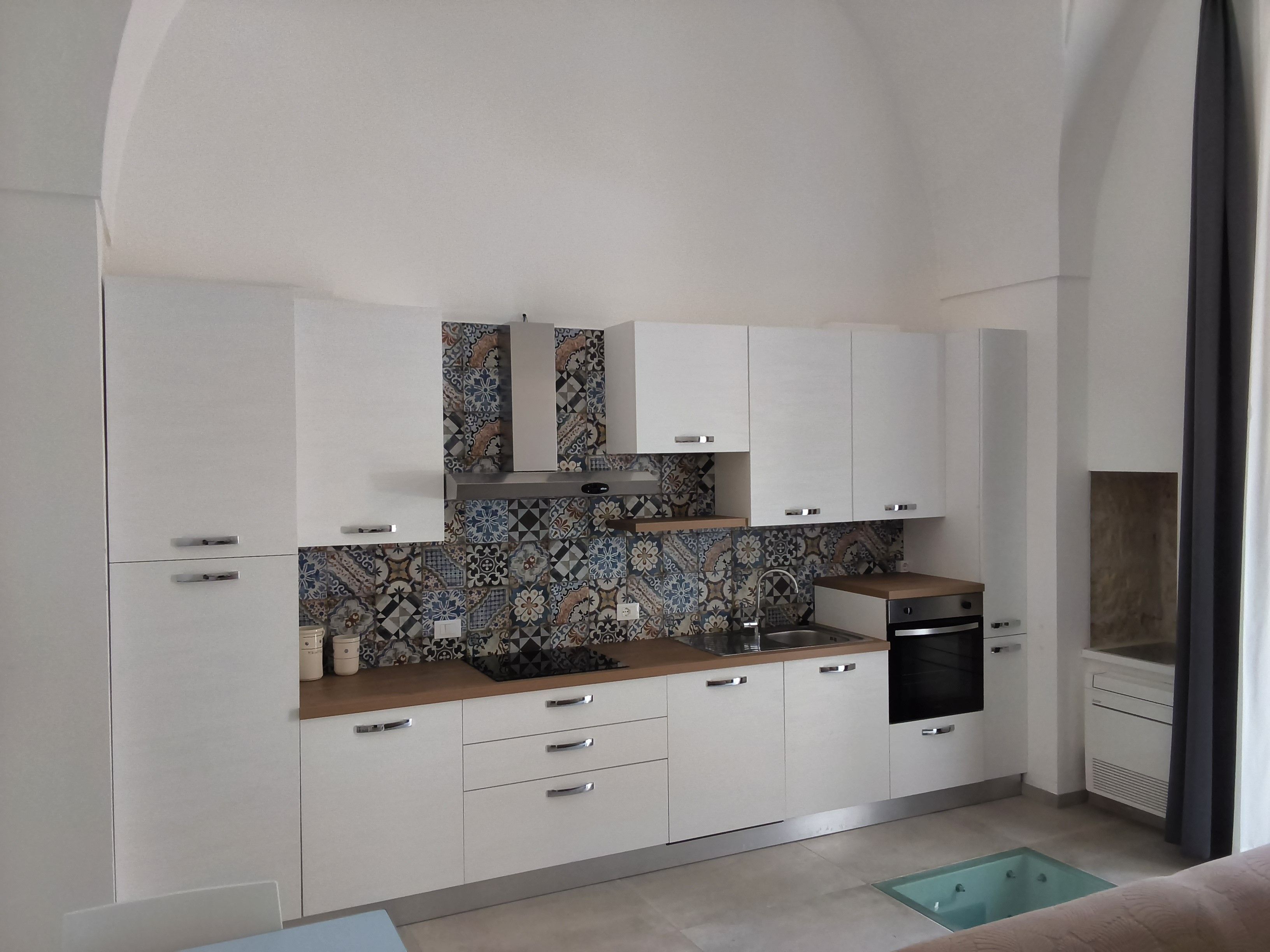 A compact kitchen with white cabinets, a patterned backsplash, and a built-in dishwasher.