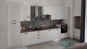 Eine kompakte Küche mit weißen Schränken, einer gemusterten Spritzschutzwand und einem integrierten Geschirrspüler.