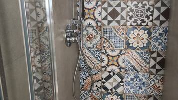 Un angolo doccia con porta in vetro e parete piastrellata decorata con motivi geometrici e floreali.