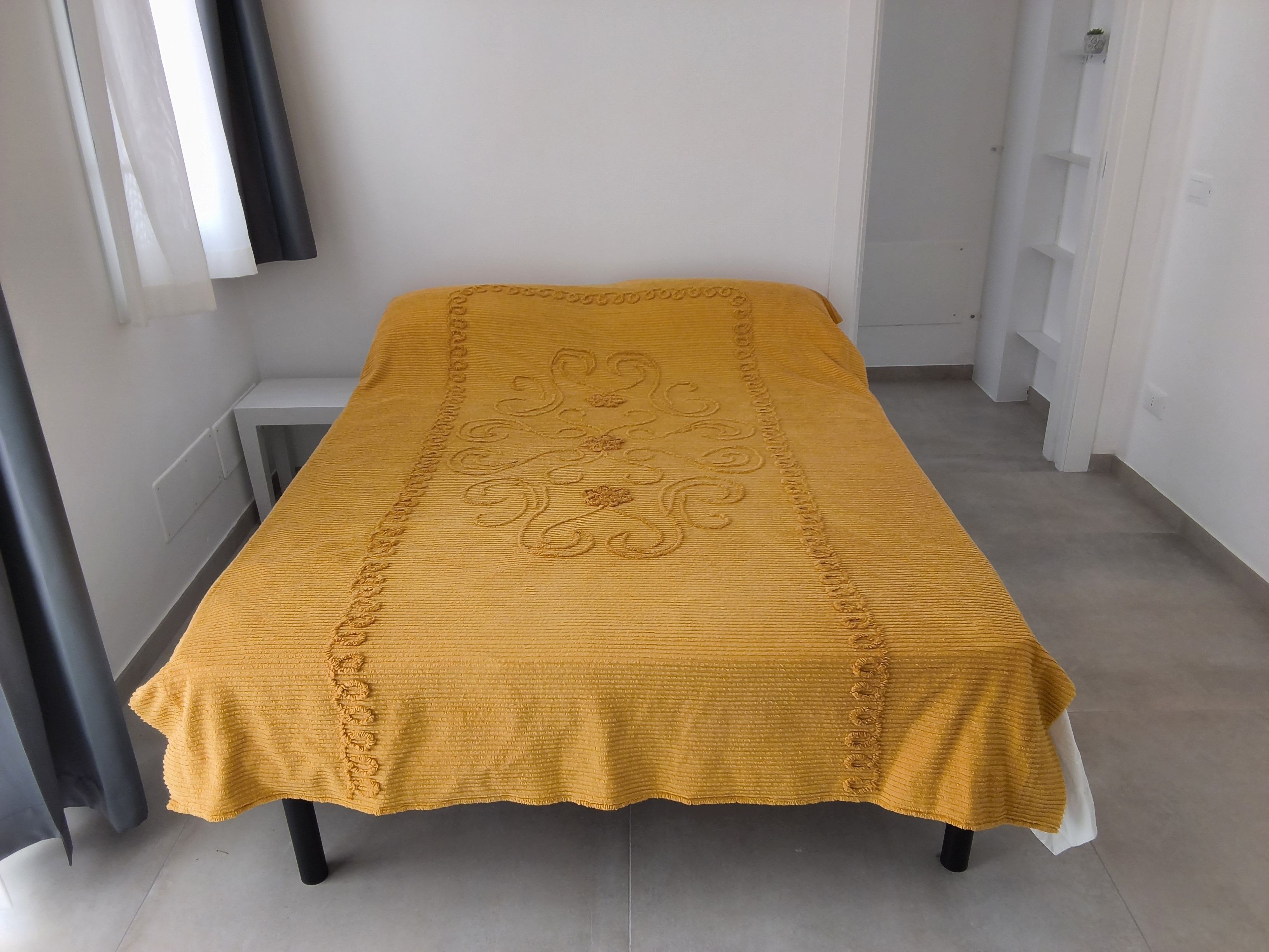 Ein Bett mit einer gelben, strukturierten Tagesdecke und einer dekorativen Kante.