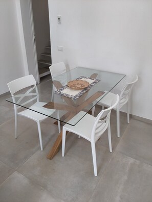 Una zona de menjador moderna amb una taula de vidre, cadires blanques i un centre decoratiu.