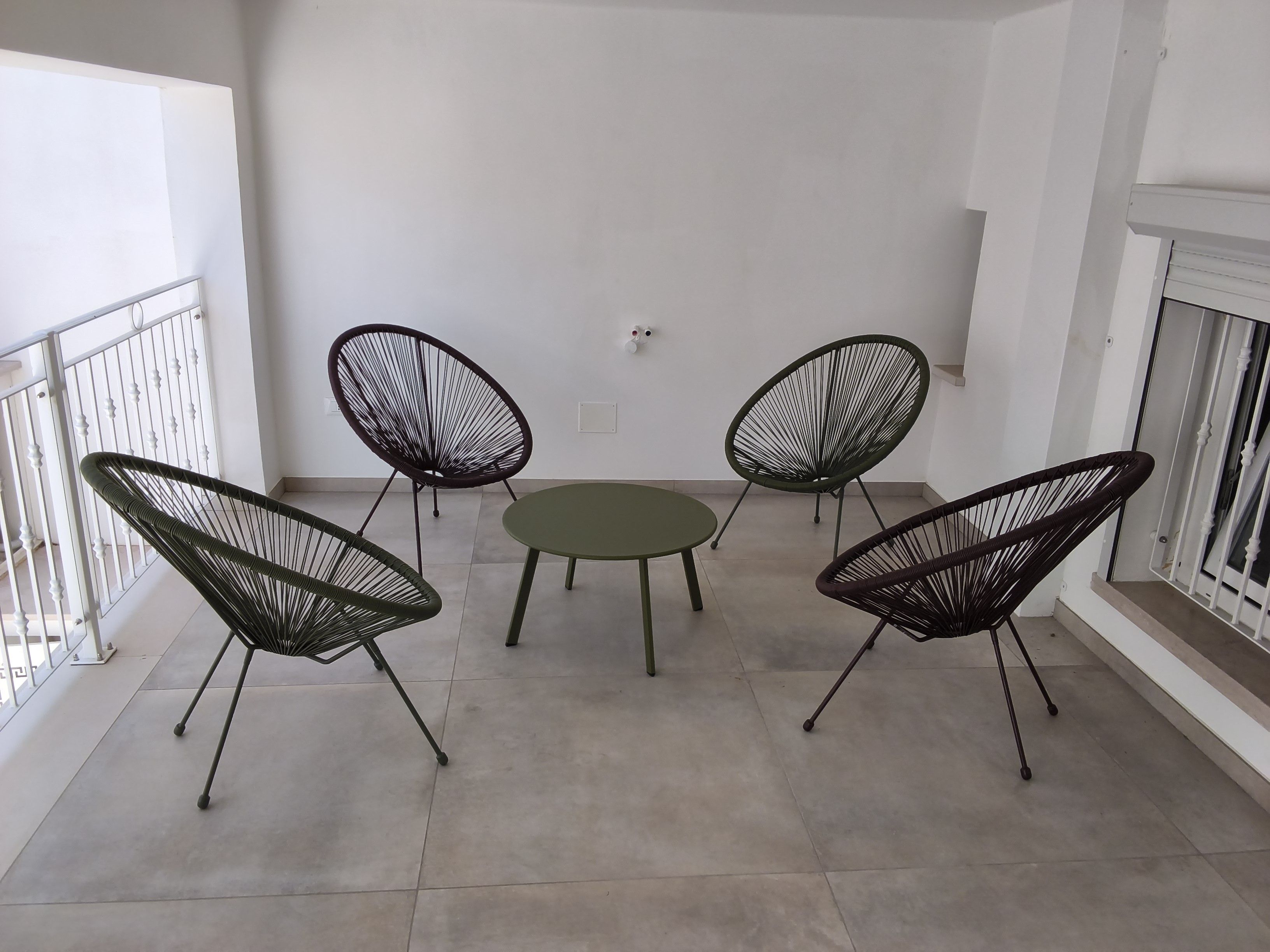 Un balcon avec une table ronde et quatre chaises, une balustrade blanche et un mur sobre.