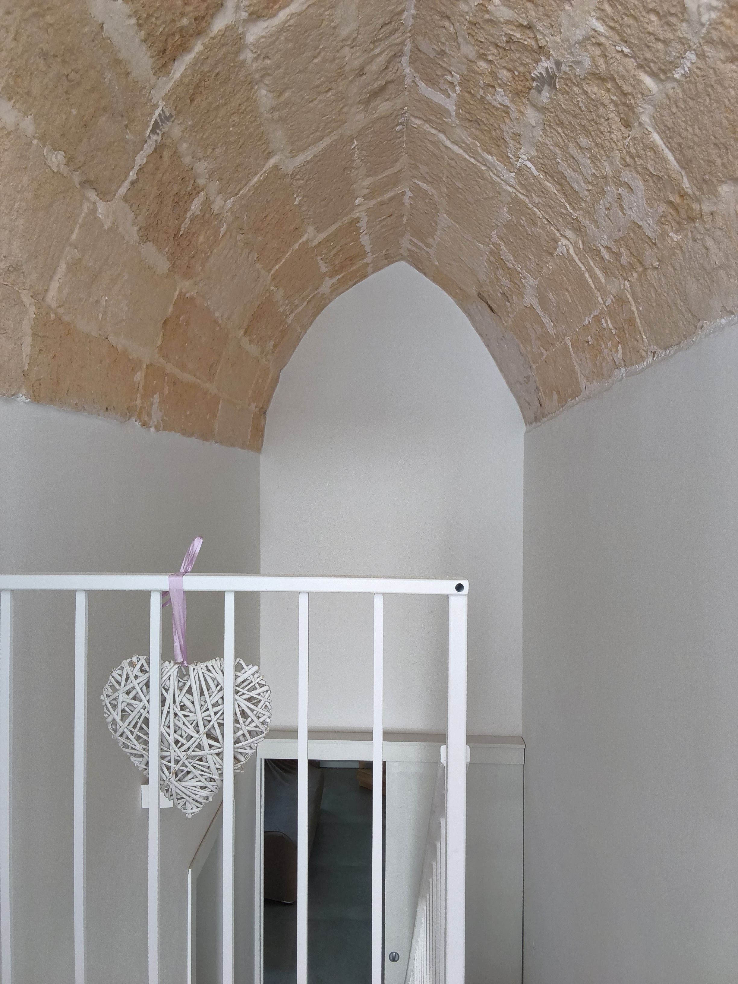 Ein Zimmer mit einem weißen Babybett, einem daran hängenden gewebten Korb und einer Ziegeldecke.
