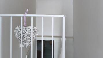 Ein Zimmer mit einem weißen Babybett, einem daran hängenden gewebten Korb und einer Ziegeldecke.