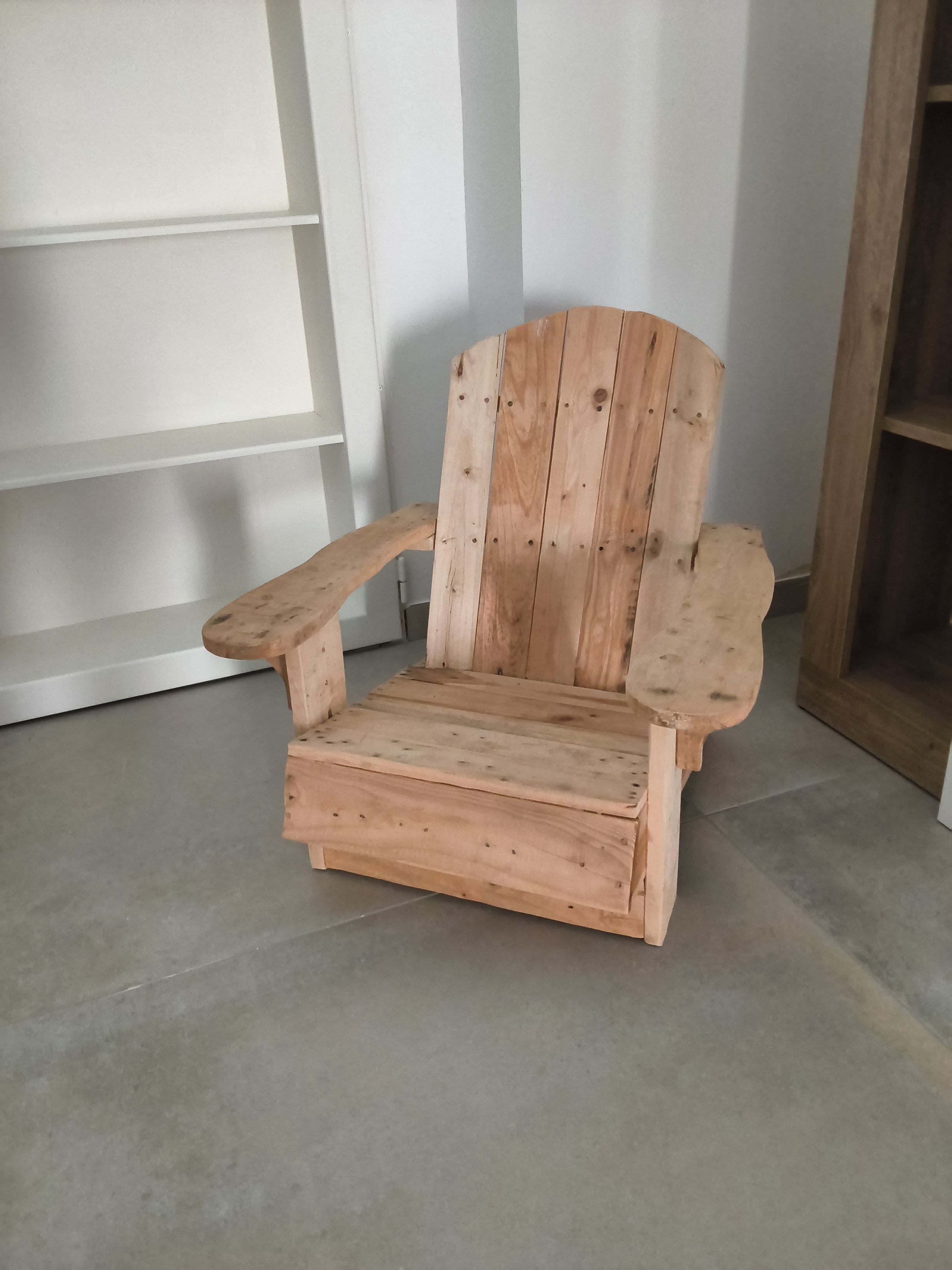 Ein hölzerner Adirondack-Stuhl mit Armlehnen und hoher Rückenlehne, auf einem gefliesten Boden platziert.