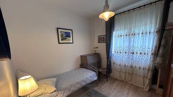 Een slaapkamer met een enkel bed, een bureau, een stoel, een lamp en een raam met gordijnen.