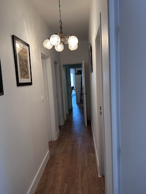 A hallway with wooden flooring, white walls, and a chandelier.