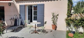 Et udendørs siddeområde med et bord, stole, en potteplante og en skydedør.
