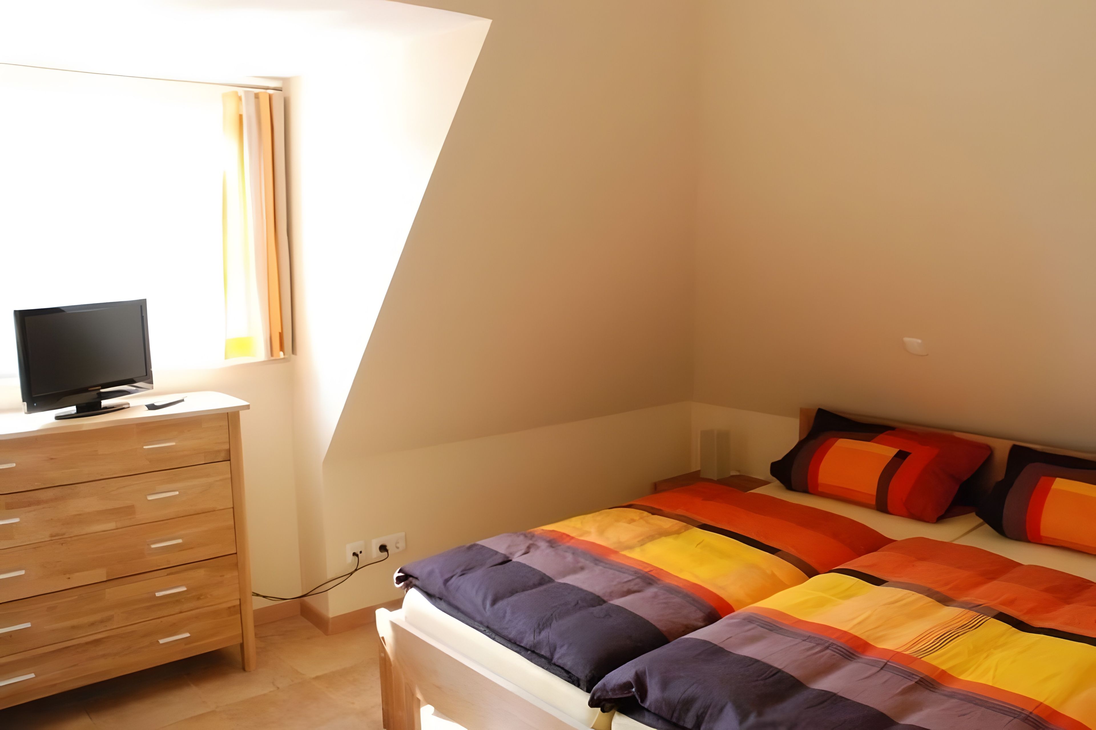Un dormitorio con una cama, un televisor en una cómoda y una ventana.