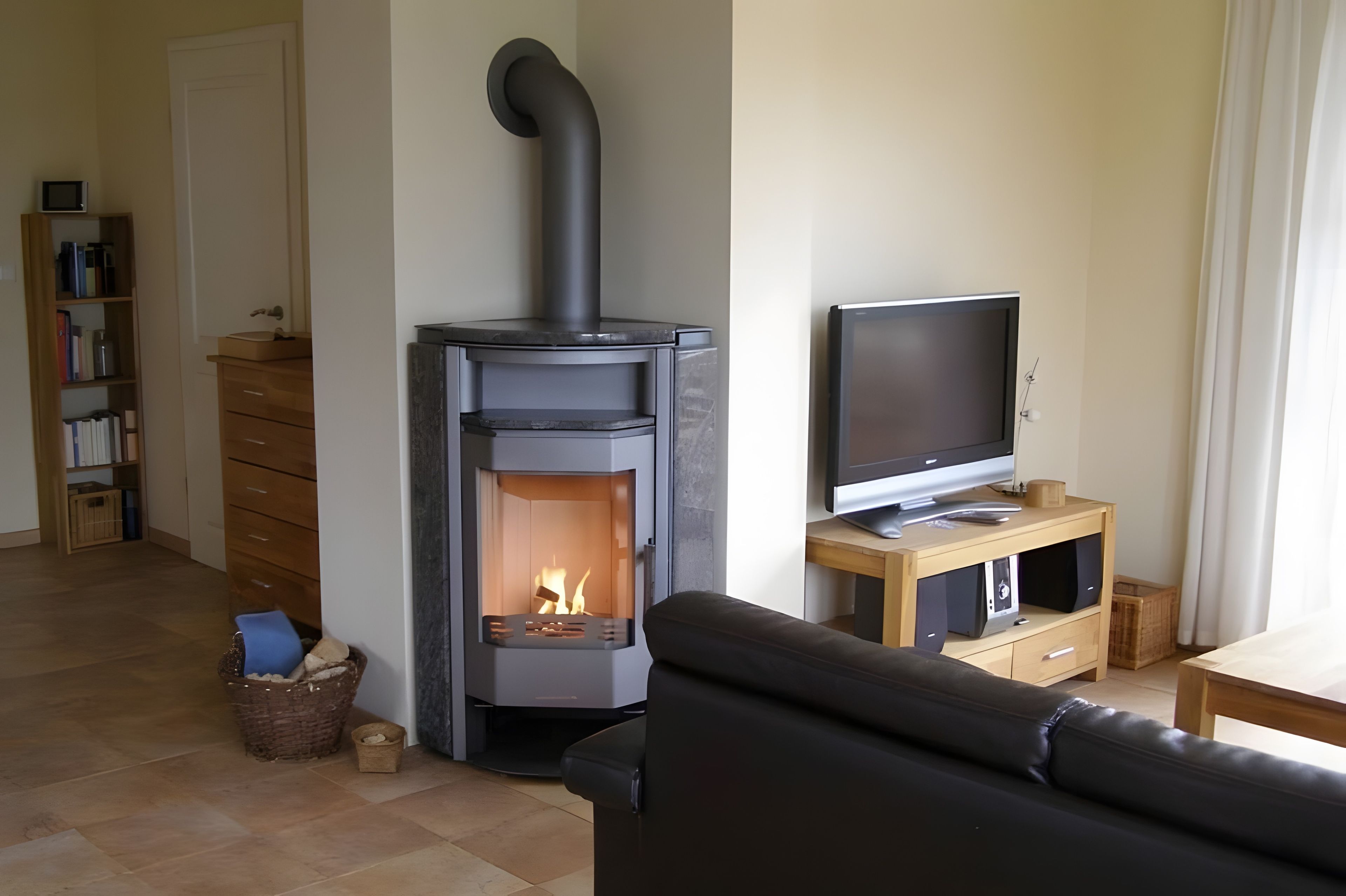 Una sala de estar con una estufa de leña, un televisor sobre un mueble de madera, un sofá y una estantería.