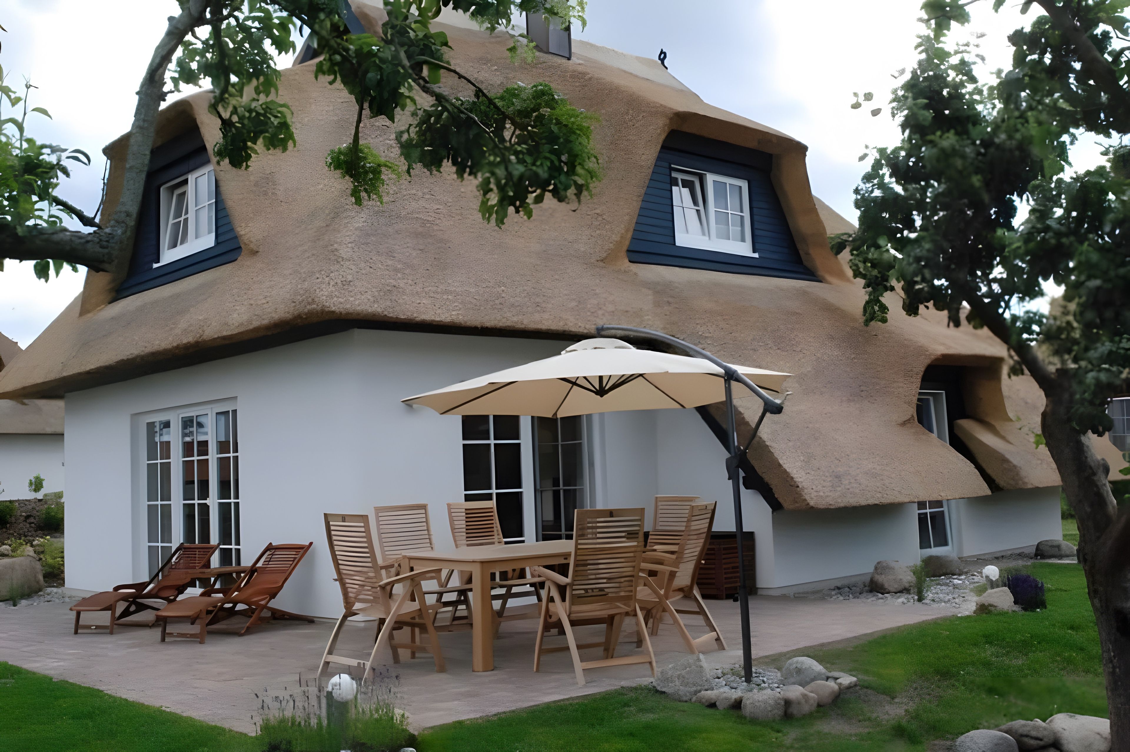 A house with a unique thatched roof and a patio area with wooden furniture and an umbrella.